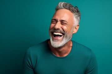 Obraz premium Portrait of a happy man in his 50s laughing over soft teal background