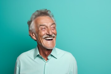 Portrait of a satisfied man in his 80s laughing in soft teal background