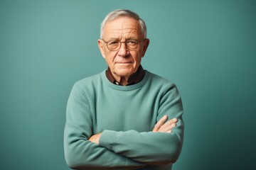 Fototapeta premium Portrait of a content man in his 70s with arms crossed in soft teal background