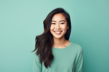 Portrait of a smiling asian woman in her 20s smiling at the camera in front of soft teal background