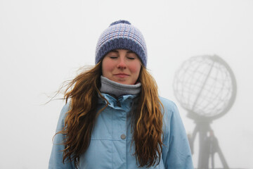 Portrait of a young traveler woman in North Cape on a foggy day, Norway. Adventure travel in...