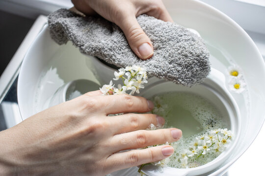 White dishes are filled with water and foam. Close-up of flowers on wet dishes. Place for text. Chamomiles in foam. Female hands washing dishes with a gray cloth. European woman