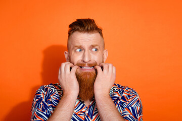 Photo of scared shocked guy dressed print shirt biting fingers looking emtpy space isolated orange...