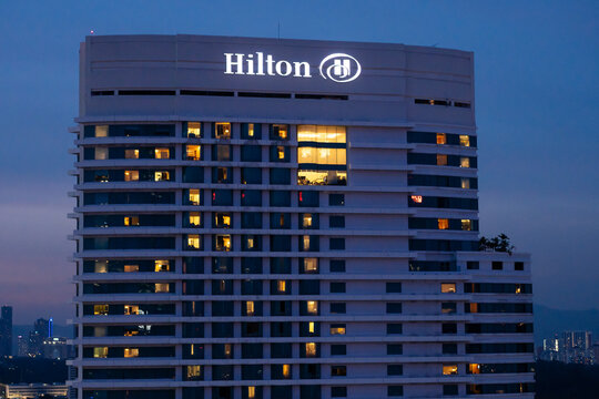 KUALA LUMPUR, MALAYSIA - JULY 16, 2023: Hilton hotel logo is illuminated against the blue hour, with some room lights shining to indicate occupancy.