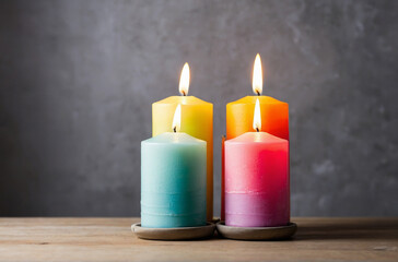 Close-up of colorful candles on a wooden table against a backdrop of a bare cement wall.