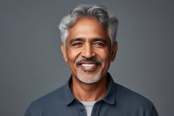 Fototapeta premium Portrait of a satisfied indian man in his 60s smiling at the camera while standing against soft gray background
