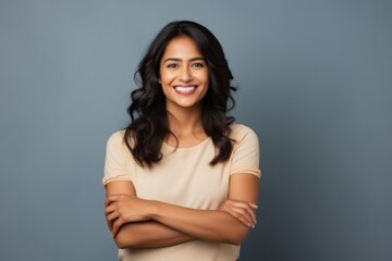 Obraz premium Portrait of a cheerful indian woman in her 20s with arms crossed in soft gray background