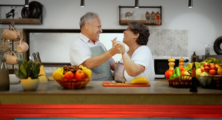 Indian Asian happy retired older senior couple pair hold hand dance modern kitchen make fun joy...