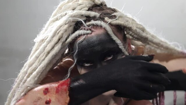 Halloween face art. Portrait of a beautiful woman looking at the camera and moving, makeup the bride's corpse. extremely long dreadlocks