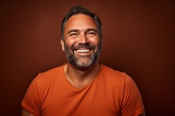Fototapeta premium Portrait of a joyful man in his 40s smiling at the camera over soft brown background