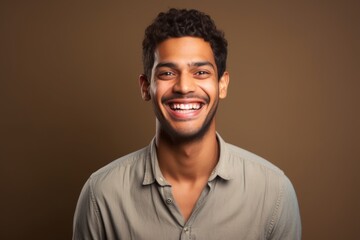 Obraz premium Portrait of a grinning indian man in his 20s smiling at the camera on soft brown background