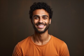 Obraz premium Portrait of a grinning indian man in his 20s smiling at the camera on soft brown background