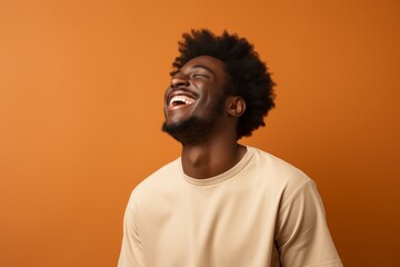 Fototapeta premium Portrait of a blissful afro-american man in his 20s laughing isolated in soft brown background