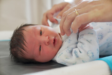 Close-up of a newborn baby wearing a white and blue patterned onesie, lying on a changing table,...