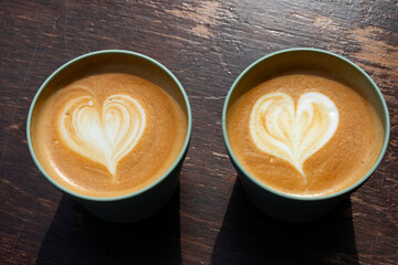 Two reusable return cups with cappuccino coffee and hearts close up