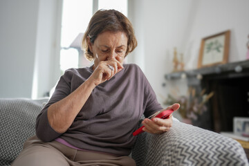 Elderly woman with short hair ironing a pair of pants on an ironing board, wearing a white sweater,...