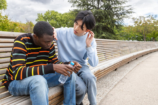 Concerned friend helping man with hypoglycemic symptoms on park bench