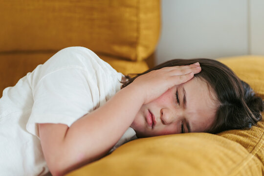 Young girl experiencing headache while resting on couch