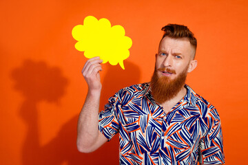 Photo of puzzled brutal guy with red beard wear print shirt holding mind cloud in arm speak isolated on vivid orange color background