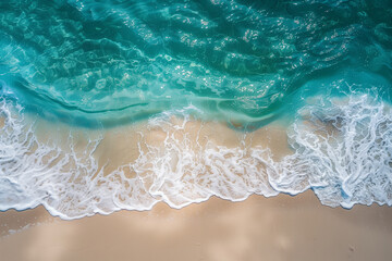 Fototapeta premium A top view of the crystal-clear azure sea, white wave foam, and beautiful sandy beach on a sunny day