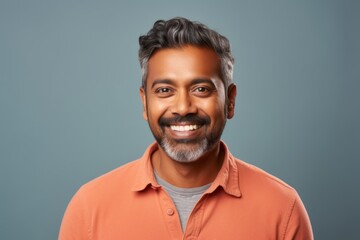 Fototapeta premium Portrait of a satisfied indian man in his 40s smiling at the camera while standing against pastel or soft colors background
