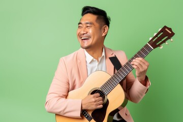 Portrait of a content asian man in his 40s playing the guitar isolated in pastel or soft colors...