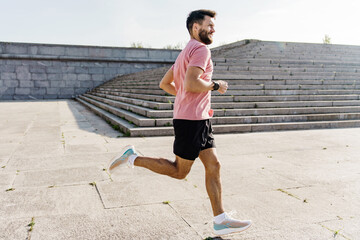 A man runs beside a set of concrete steps on a waterfront promenade. He is dressed in athletic...