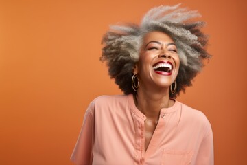 Portrait of a merry afro-american woman in her 60s laughing in pastel or soft colors background