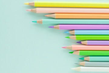 Pastel colored pencils in uneven row on a light blue background