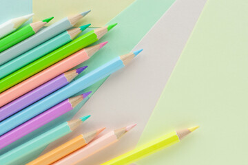 Pastel colored pencils in uneven row on sheets of colored paper
