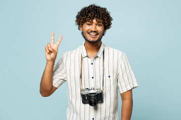 Traveler smiling Indian man wears white casual clothes showing victory sign isolated on plain blue...