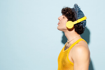 Side view young happy gay Latin man wear mesh tank top hat clothes listen to music in headphones...