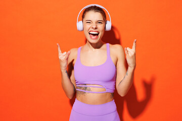 Young cool fun fitness trainer instructor sporty woman sportsman wear purple top clothes in home gym listen to music in headphones isolated on plain orange background. Workout sport fit abs concept.