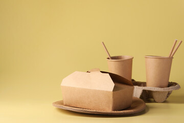 Eco friendly food packaging. Paper containers, cardboard cup holder and straws on pale yellow background, space for text