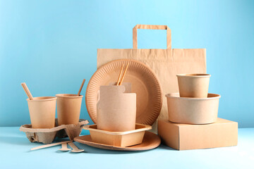 Eco friendly food packaging. Paper containers, tableware and bag on white table against light blue...