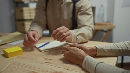 An empathetic detective comforts a woman, taking notes in a nondescript police station room with visible evidence, case files, and indoor wooden furnishings.