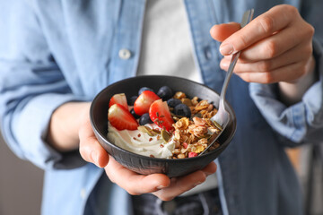 Woman eating tasty granola with berries, yogurt and seeds, closeup