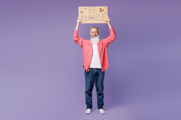 Full body elderly bearded gay man 50s years old wears pink shirt casual clothes hold card with be yourself title text look aside isolated on plain purple background. Lifestyle LGBT June pride concept.