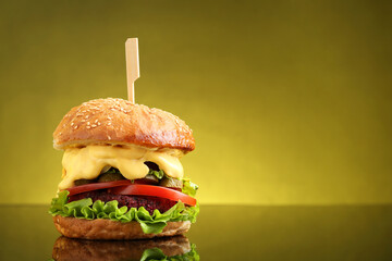 Delicious vegetarian burger on mirror surface against olive background, space for text