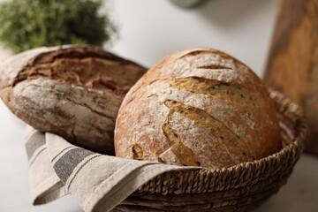 Wicker bread basket with freshly baked loaves on table in kitchen, closeup