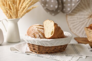 Wicker bread basket with freshly baked loaf on white marble table in kitchen