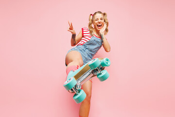 Bottom view young fun woman wear red t-shirt denim overalls casual clothes blue rollers rollerblading stretch close up leg to camera isolated on plain pink background. Summer sport lifestyle concept.