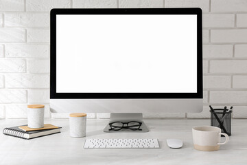 Fototapeta premium Office workplace with computer, cup and stationery on light table near white brick wall