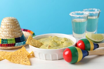 Delicious guacamole with nachos chips, Mexican sombrero hat, maracas and tequila on white wooden...