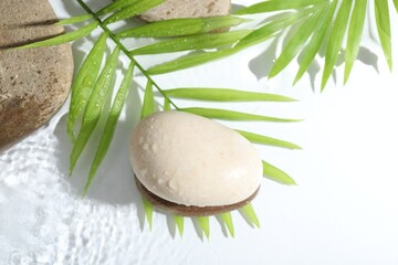 Spa stones and palm leaves in water on white background
