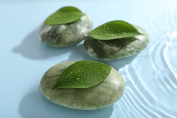 Spa stones and green leaves on light blue background, closeup
