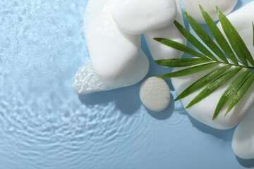 Spa stones and palm leaf in water on light blue background, flat lay. Space for text