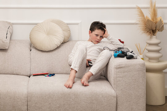 Boy lounging on couch with toys and game controller