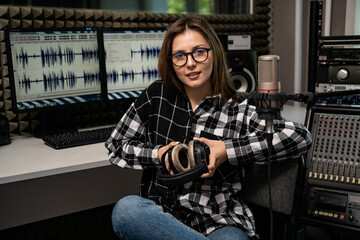 cute girl sound engineer with headphones in her hands sits in a recording studio. Workplace portrait.