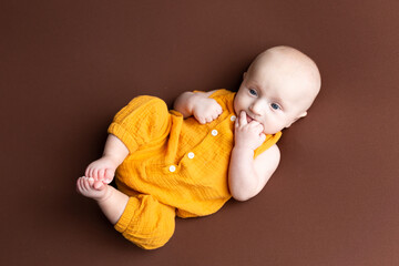 small child sucking fingers on a brown background. portrait of a newborn boy. baby's first photo...